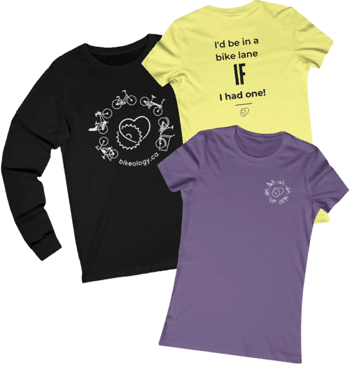 Three different bikeology shirts layered on top of eachother. One is a black longsleeve with the bikeology dot c a logo in white on the chest. One is yellow with a quote on the back that reads: I'd be in a bike lane if I had one! The other is purple with a small bikeology logo on the left breast. Three different bikeology shirts layered on top of eachother. One is a black longsleeve with the bikeology dot c a logo in white on the chest. One is yellow with a quote on the back that reads: I'd be in a bike lane if I had one! The other is purple with a small bikeology logo on the left breast.